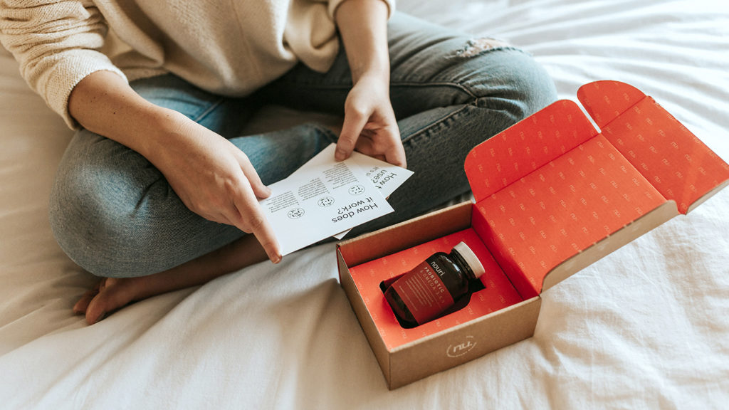 Packaging design for a wellness brand that is being unpacked by a woman sitting on a comfy bed.